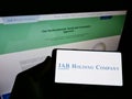 Person holding smartphone with logo of business conglomerate JAB Holding Company S.ÃÂ  r.l. on screen in front of webpage.